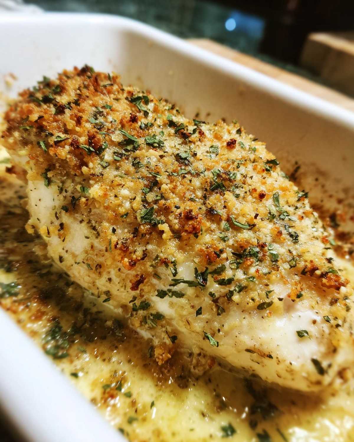 Close-up of a juicy chicken breast with a golden, herbed, breadcrumb topping in a creamy sauce, ready for the Garlic parmesan chicken bake.