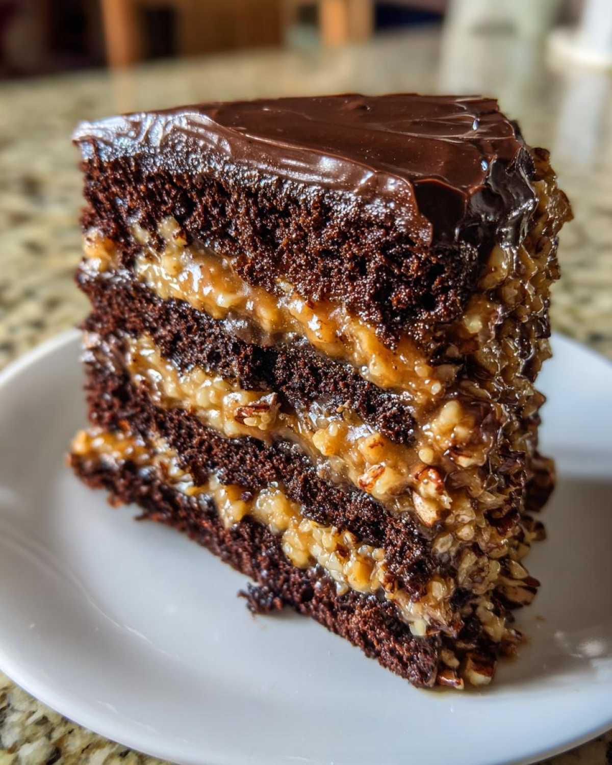 A close-up slice of rich german chocolate cake showing dark layers, coconut-pecan filling, and chocolate ganache topping.