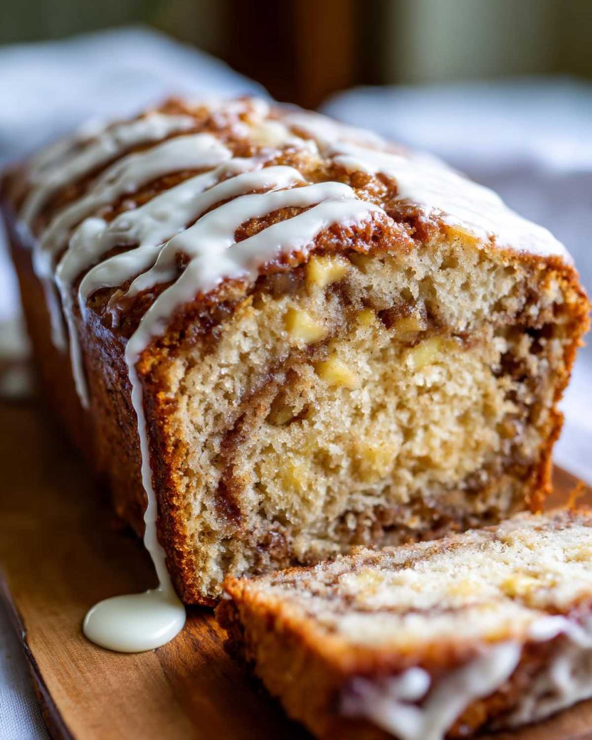 Close-up of a freshly baked apple fritter bread loaf drizzled with white glaze, with one slice cut.