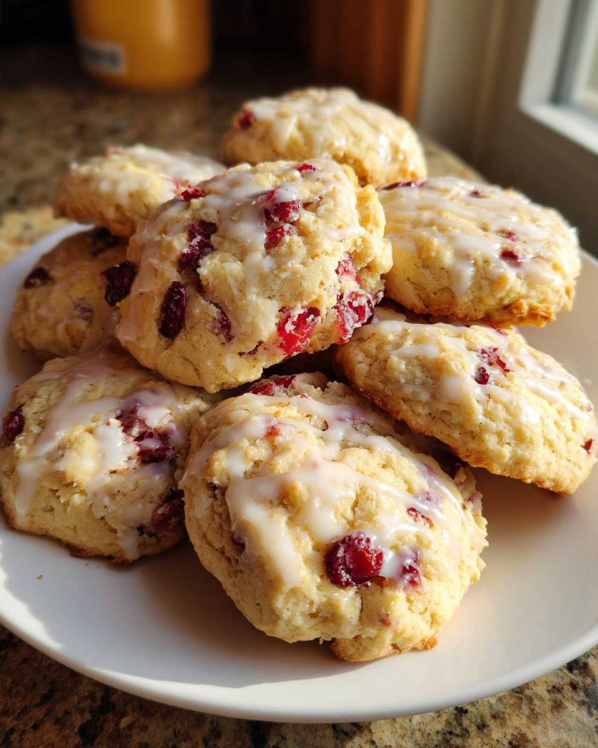 A stack of freshly baked cranberry orange cookies drizzled with white glaze, sitting on a white plate.