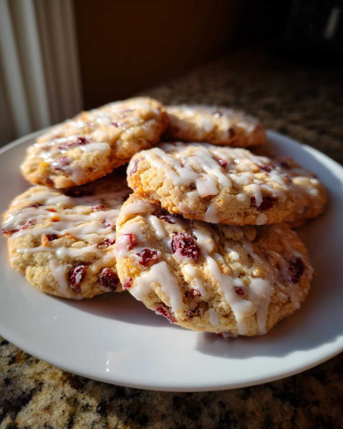 A stack of freshly baked cranberry orange cookies drizzled with white glaze, sitting on a white plate.