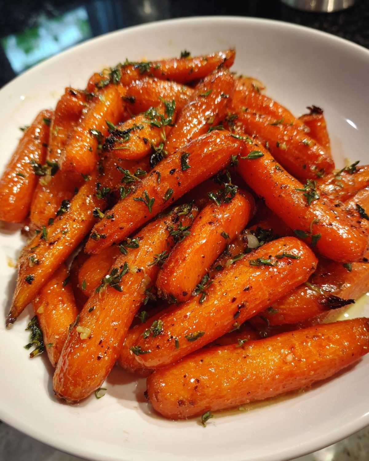 Close-up of shiny, glazed roasted carrots topped with fresh herbs and garlic, ready to serve.