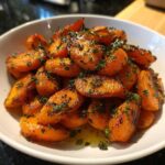 Close-up of perfectly glazed roasted carrots tossed with fresh chopped herbs in a white serving bowl.