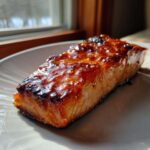 A perfectly cooked, thick fillet of salmon with a rich, dark, glossy glaze, highlighting the steakhouse flavor.