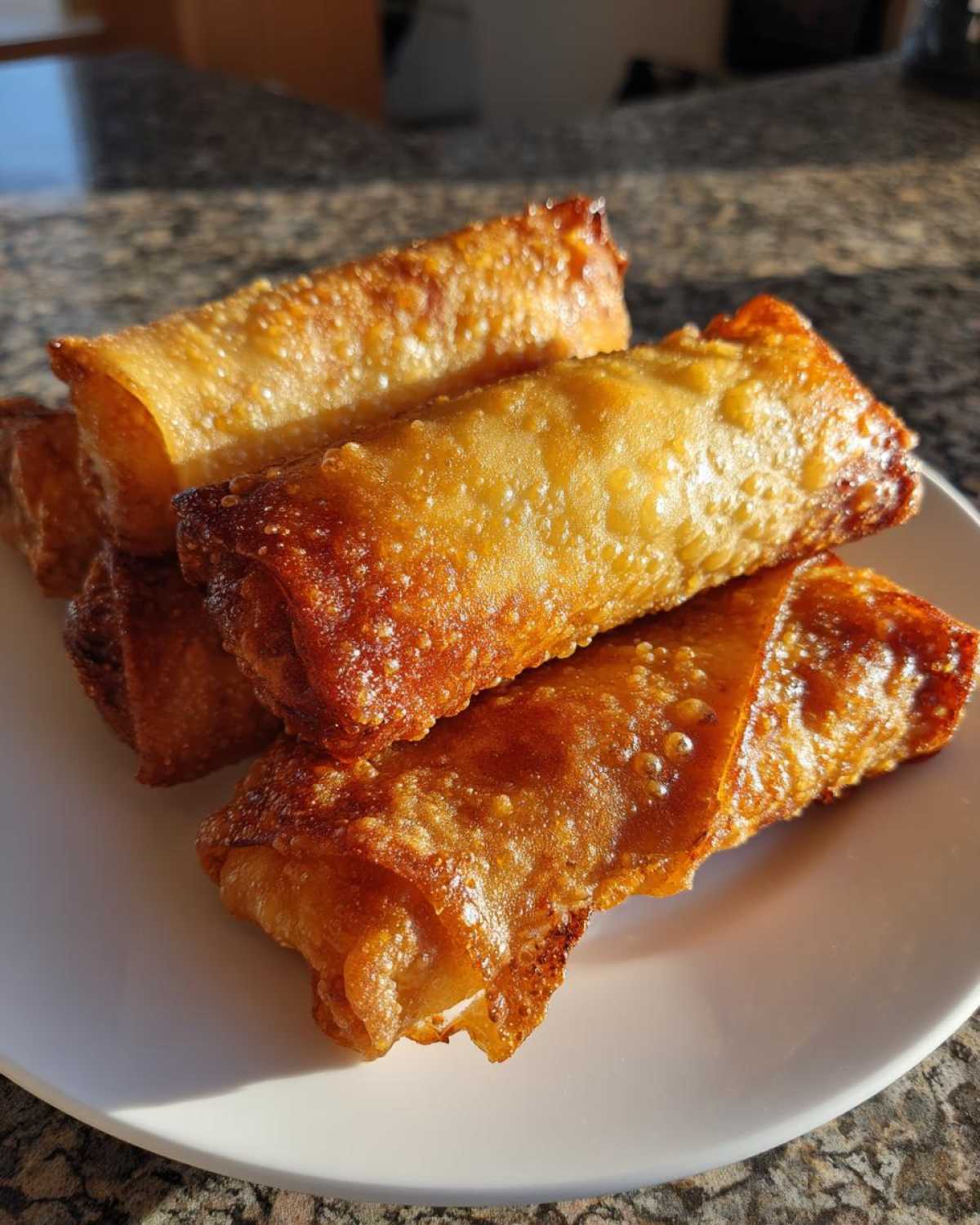 A stack of four perfectly fried, golden brown egg roll appetizers resting on a white plate.