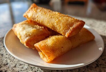 A stack of four crispy, golden brown homemade egg roll appetizers resting on a small white plate.