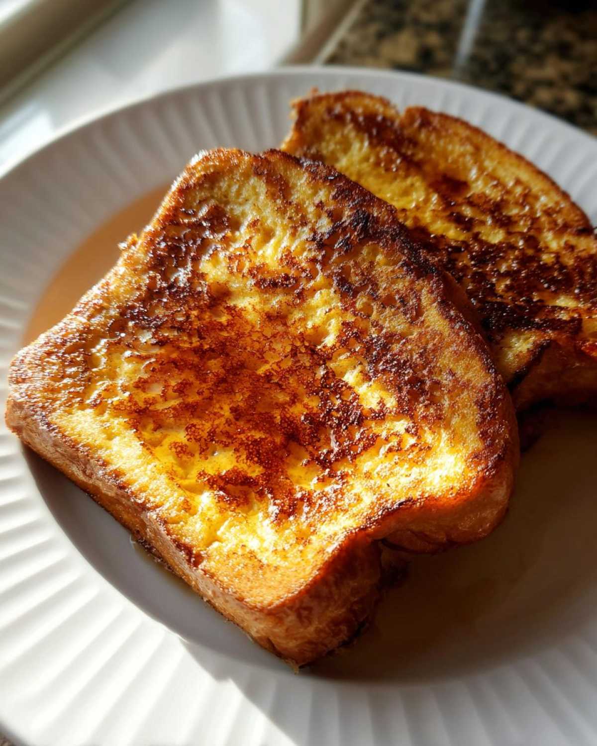 Two golden brown slices of perfectly cooked french toast drizzled with syrup on a white plate.