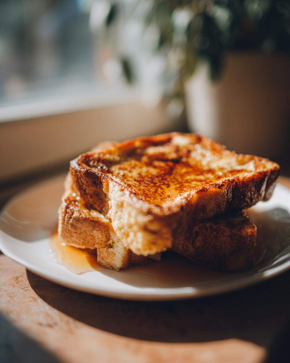 Two thick slices of golden brown french toast stacked on a white plate, drizzled generously with syrup.