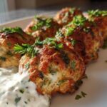 Close-up of perfectly browned greek chicken meatballs served with a dollop of creamy tzatziki sauce and fresh parsley.