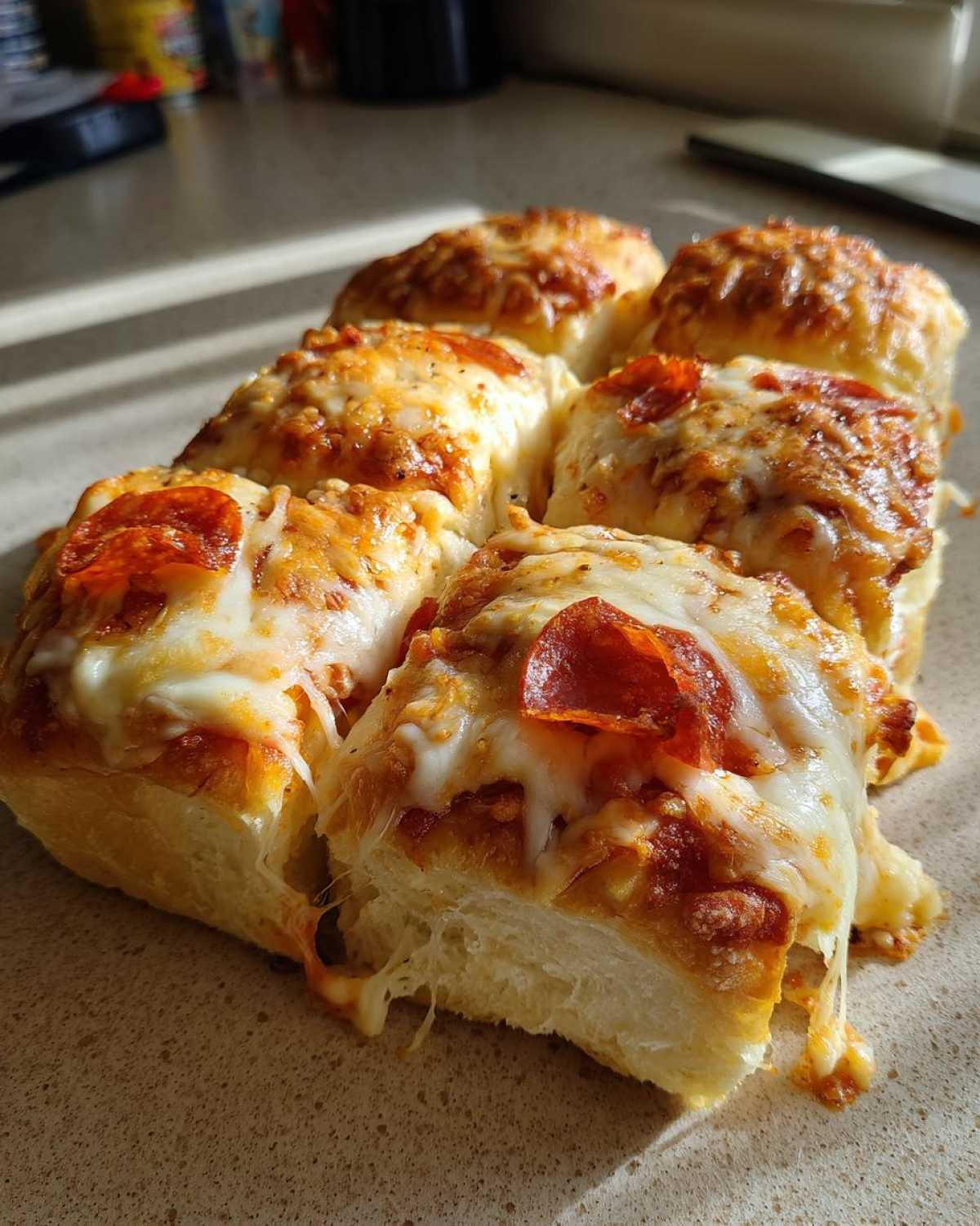 Close-up of six freshly baked pepperoni pizza sliders with melted, gooey cheese.