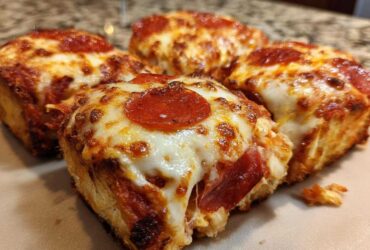 Close-up of four gooey pepperoni pizza sliders with melted, browned cheese on a light surface.