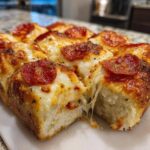 Close-up of freshly baked pizza sliders showing a dramatic cheese pull between two cut squares.
