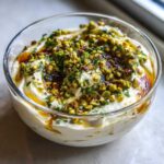 Close-up of a creamy ricotta dip topped with chopped pistachios, herbs, and a drizzle of honey or oil.