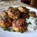 A plate of perfectly browned greek chicken meatballs garnished with fresh parsley and a side of creamy tzatziki sauce.