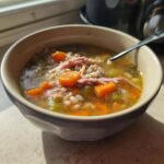 A close-up of a bowl filled with hot ham and bean soup, featuring shredded ham, carrots, celery, and beans.