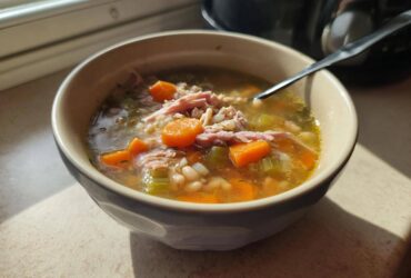 A close-up of a bowl filled with hot ham and bean soup, featuring shredded ham, carrots, celery, and beans.