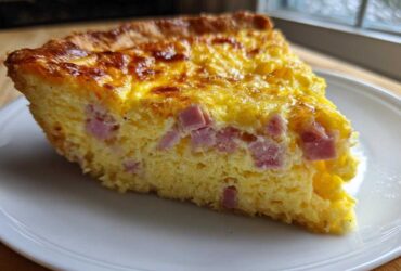 Close-up of a thick slice of ham and cheese quiche with a golden, baked top, served on a white plate.