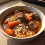 Close-up of a white bowl filled with rich beef barley soup featuring tender beef chunks, bright carrots, and plump barley.