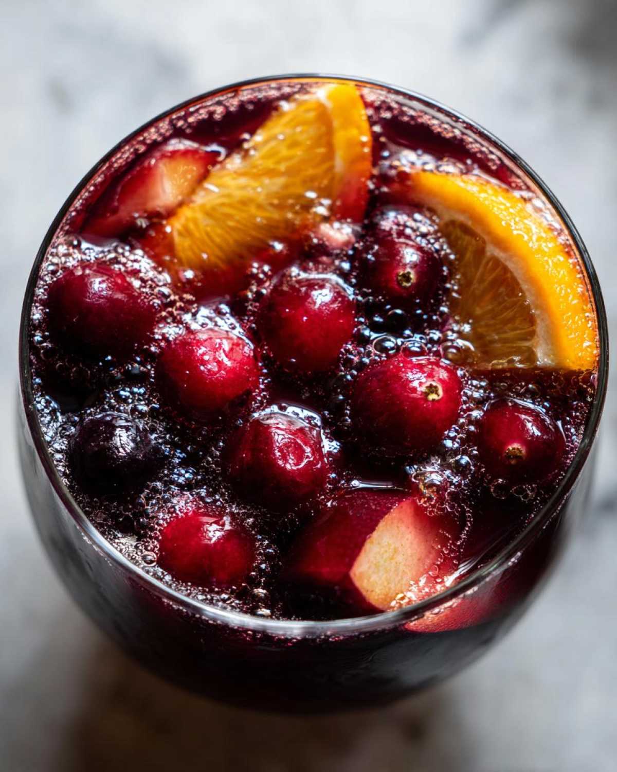 Overhead view of a glass filled with bubbling holiday sangria, featuring whole cranberries and orange slices.
