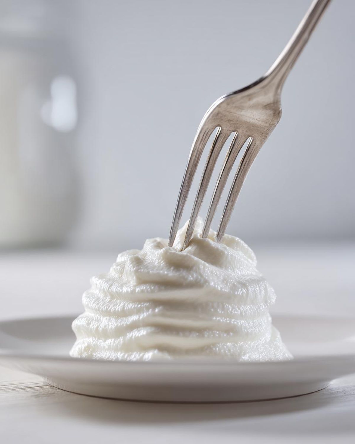 A swirl of thick, white homemade alfredo sauce being tested with a silver fork on a white plate.