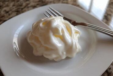A thick, creamy swirl of homemade alfredo sauce served on a small white square plate next to a fork.