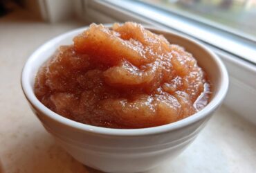 Close-up of chunky, spiced applesauce served in a small white bowl near a window.
