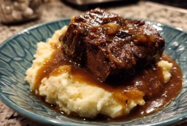 A serving of mashed potatoes topped with a piece of braised meat and rich homemade brown gravy.