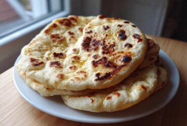 A stack of fluffy, slightly charred homemade naan bread glistening with butter on a white plate.