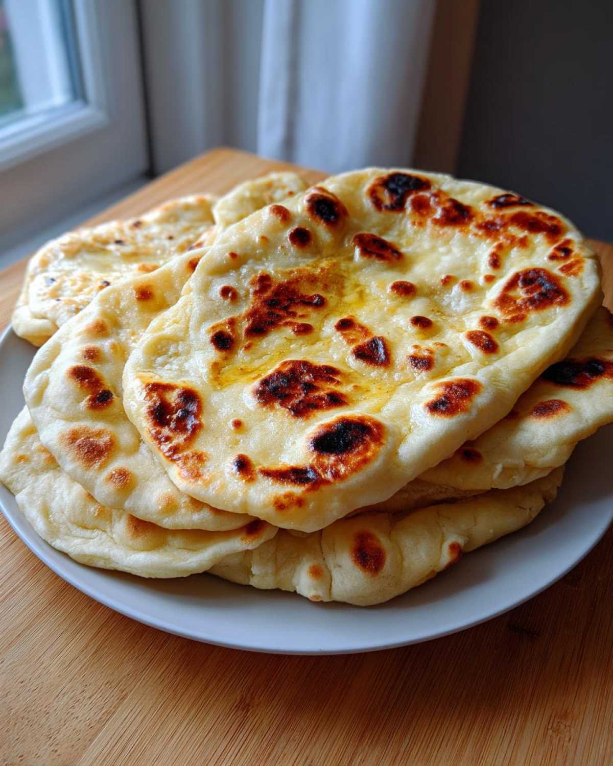 A stack of fluffy, golden homemade naan bread brushed with melted butter, showing charred spots.