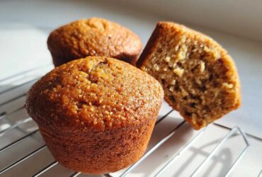 Three golden brown honey bran muffins cooling on a wire rack, one is cut in half showing the moist interior.