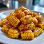 Close-up of sweet, glazed honey butter corn pieces piled high on a white plate.