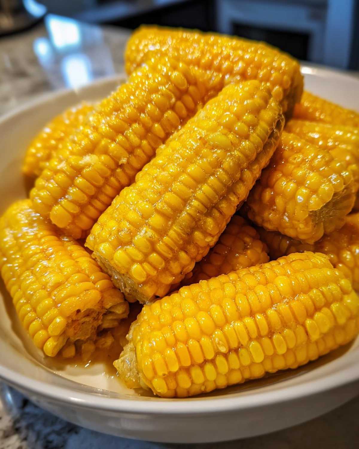 Close-up of several bright yellow cobs of corn glistening with honey butter in a white bowl.