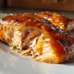 Close-up of a flaky, glazed piece of honey garlic salmon on a white plate.