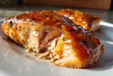 Close-up of a flaky, glazed piece of honey garlic salmon on a white plate.