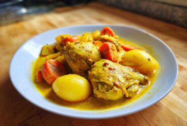 A close-up of Jamaican curry chicken pieces in a rich yellow sauce with potatoes and carrots.