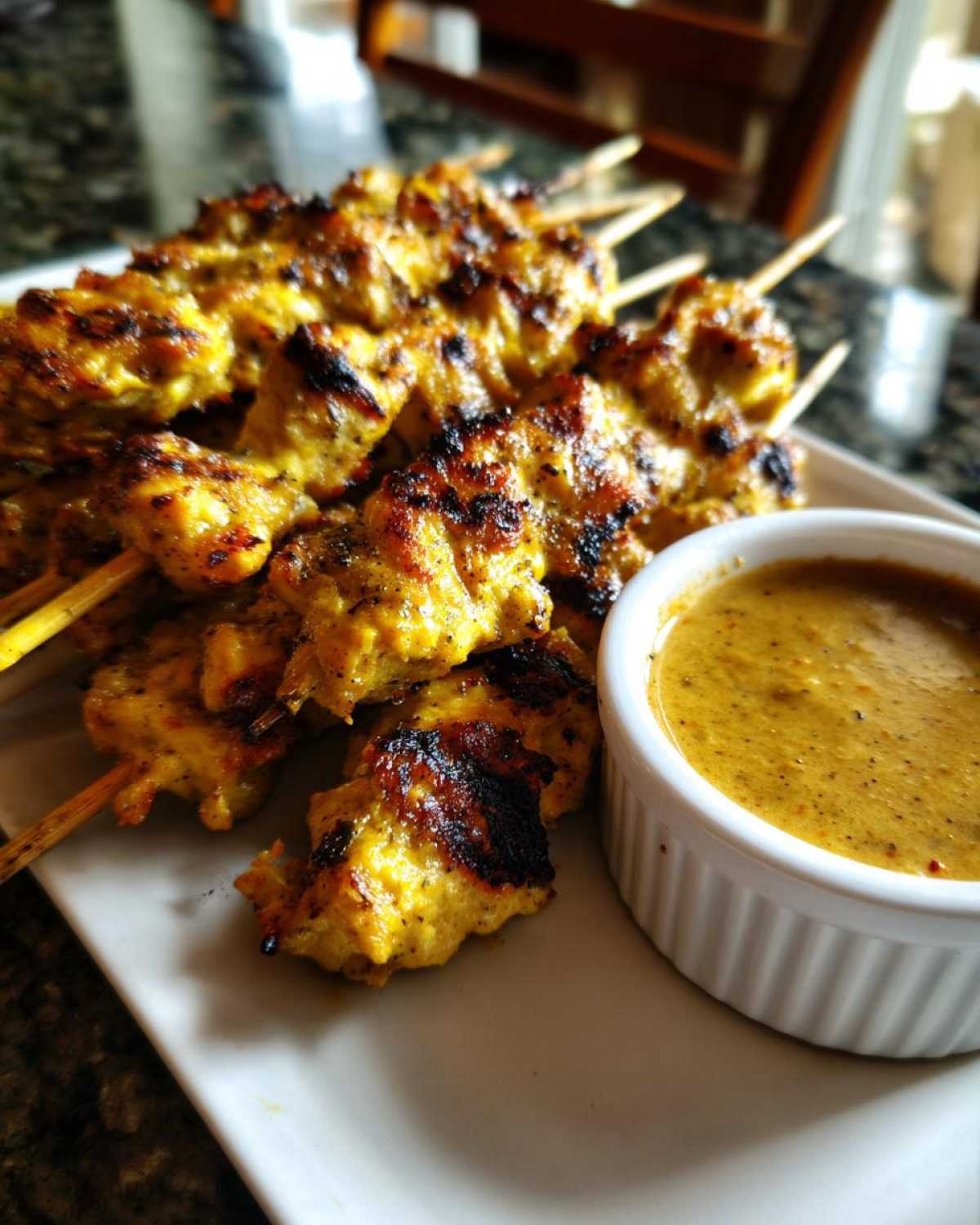 Close-up of perfectly grilled chicken satay skewers served with a side of rich peanut sauce.