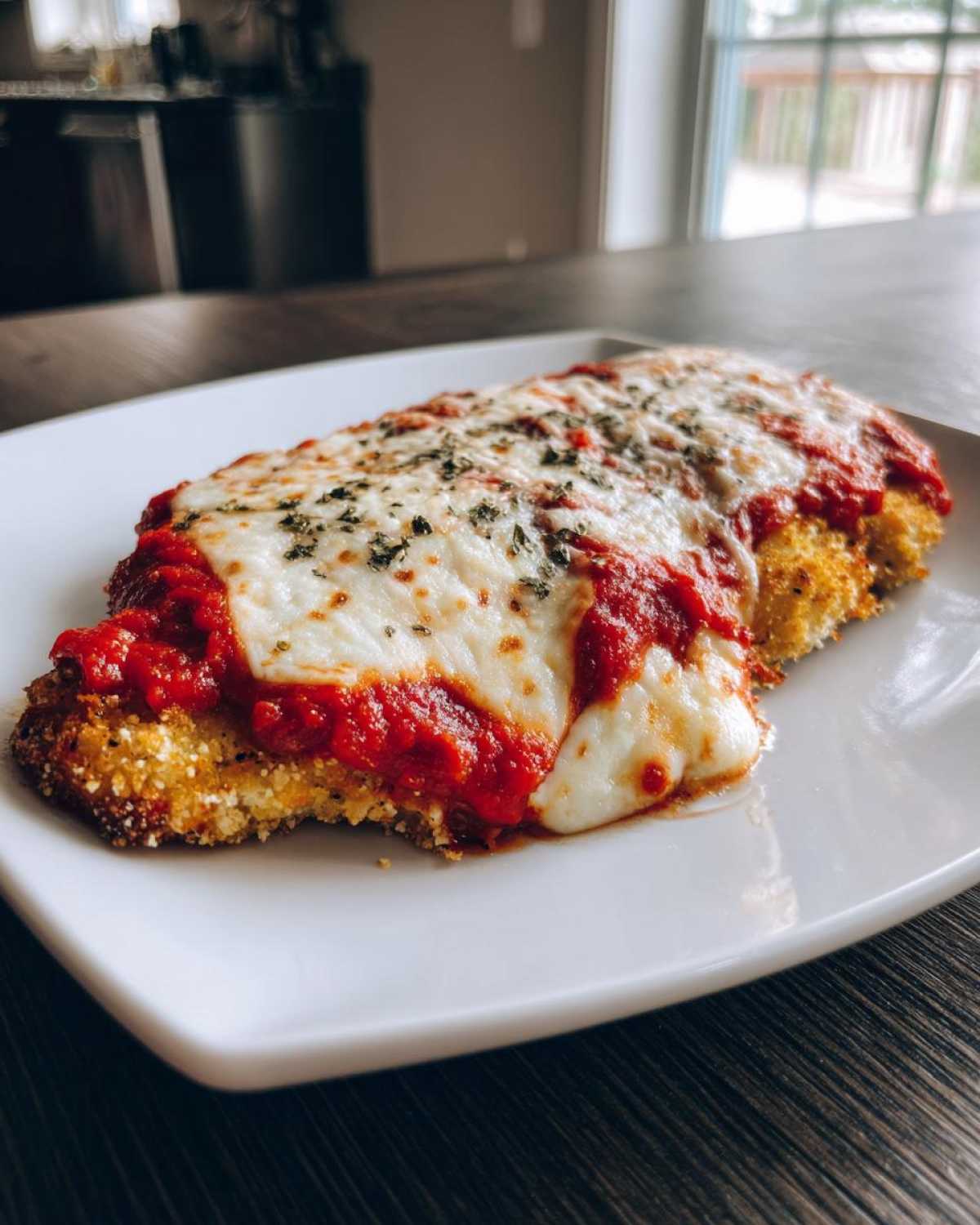 A close-up of a breaded chicken breast topped with marinara sauce and melted mozzarella cheese, representing keto chicken parmesan.