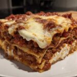 A thick, layered slice of lasagna with cottage cheese, meat sauce, and melted cheese topping.