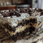 A close-up view showing the layers of creamy filling and crushed cookies in a glass dish of oreo dirt cake.
