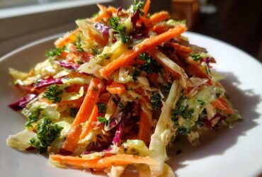 A mound of vibrant cabbage salad featuring shredded carrots, red cabbage, and fresh parsley, served on a white plate.