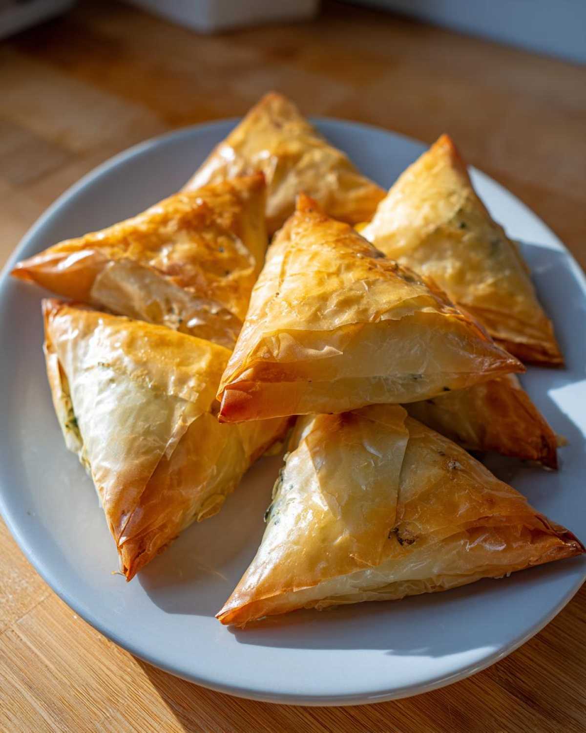 A plate piled high with golden brown, crispy Mediterranean Spinach and Feta Cheese Crisps triangles.