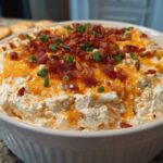 A close-up of creamy Million Dollar Dip topped with melted cheddar cheese, crispy bacon bits, and fresh chives.