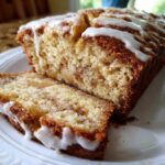 Close-up of sliced apple fritter bread drizzled with white vanilla glaze on a white plate.