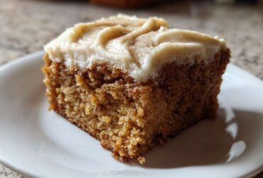 Close-up of a moist slice of applesauce cake topped with thick cream cheese frosting and a sprinkle of cinnamon.