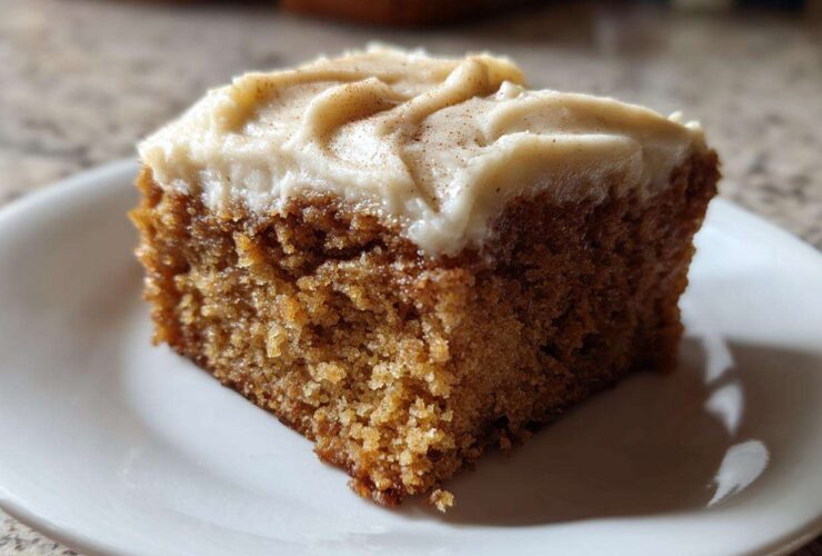 Close-up of a moist slice of applesauce cake topped with thick cream cheese frosting and a sprinkle of cinnamon.
