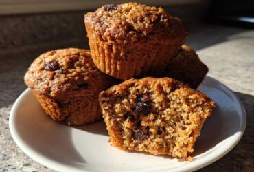 A stack of moist bran muffins, one broken open to show the texture and raisins inside.