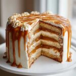 A tall, moist caramel cake with four layers, filled with cream and caramel, covered in white frosting and a heavy caramel drip.