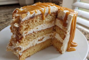 Close-up of a slice of moist caramel cake showing three layers of cake and frosting, topped with thick caramel drizzle.
