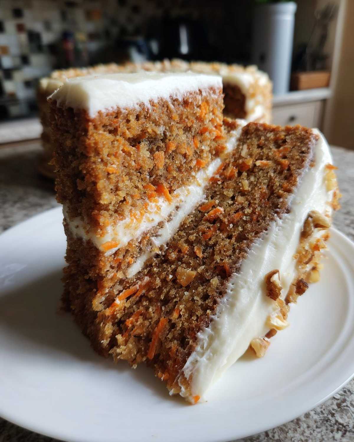 Close-up of two slices of moist carrot cake recipe with thick cream cheese frosting and pecans.