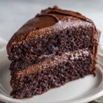 Close-up of a rich, moist slice of chocolate cake recipe covered in thick, glossy dark chocolate frosting.